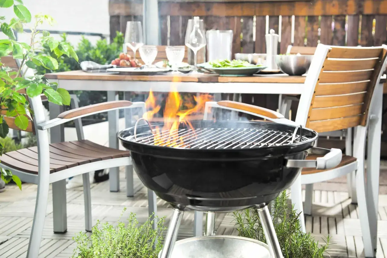 La grille bbq est prête pour un festin en plein air. Des flammes dansent sur les braises, promettant des saveurs estivales. La table est dressée, invitant au partage.