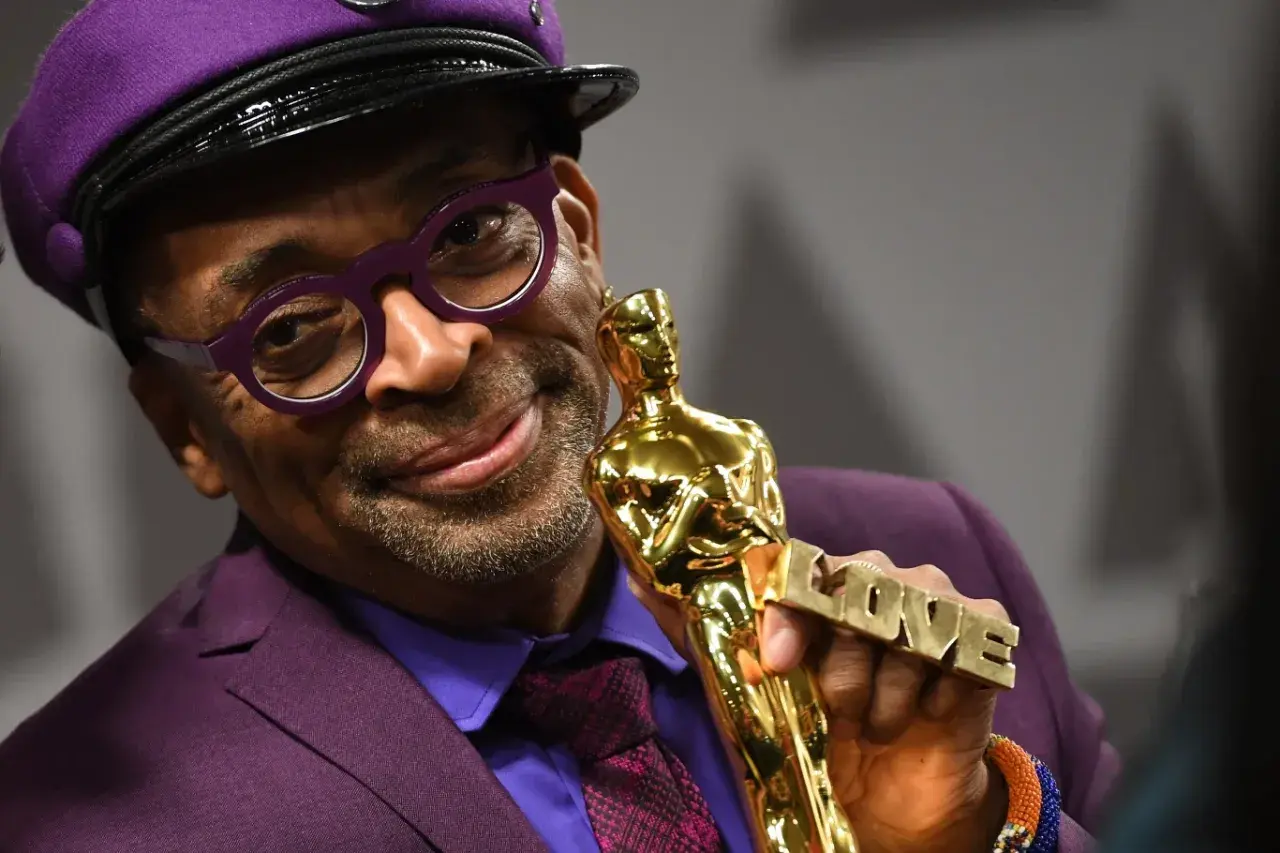 Spike Lee, w fioletowym garniturze i czapce, trzyma Oscara z napisem "LOVE". Jego filmy często poruszają ważne tematy społeczne.