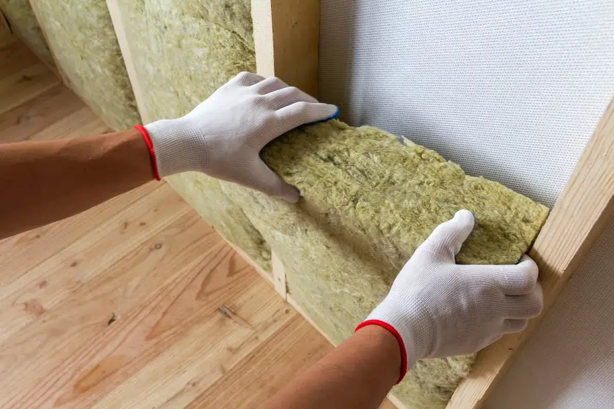 Mains gantées installant un isolant minéral dans une structure en bois pour une isolation intérieure efficace.