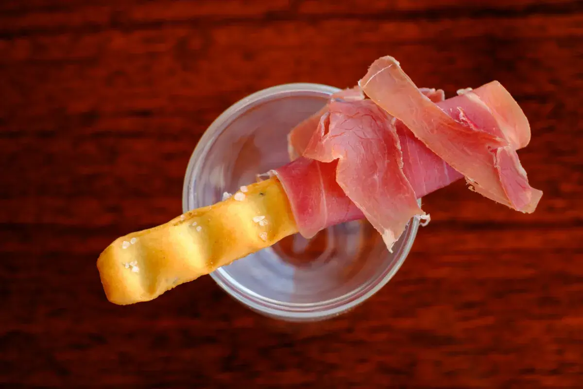 Ein knuspriger Grissini mit zartem Schinken, serviert in einem Glas.