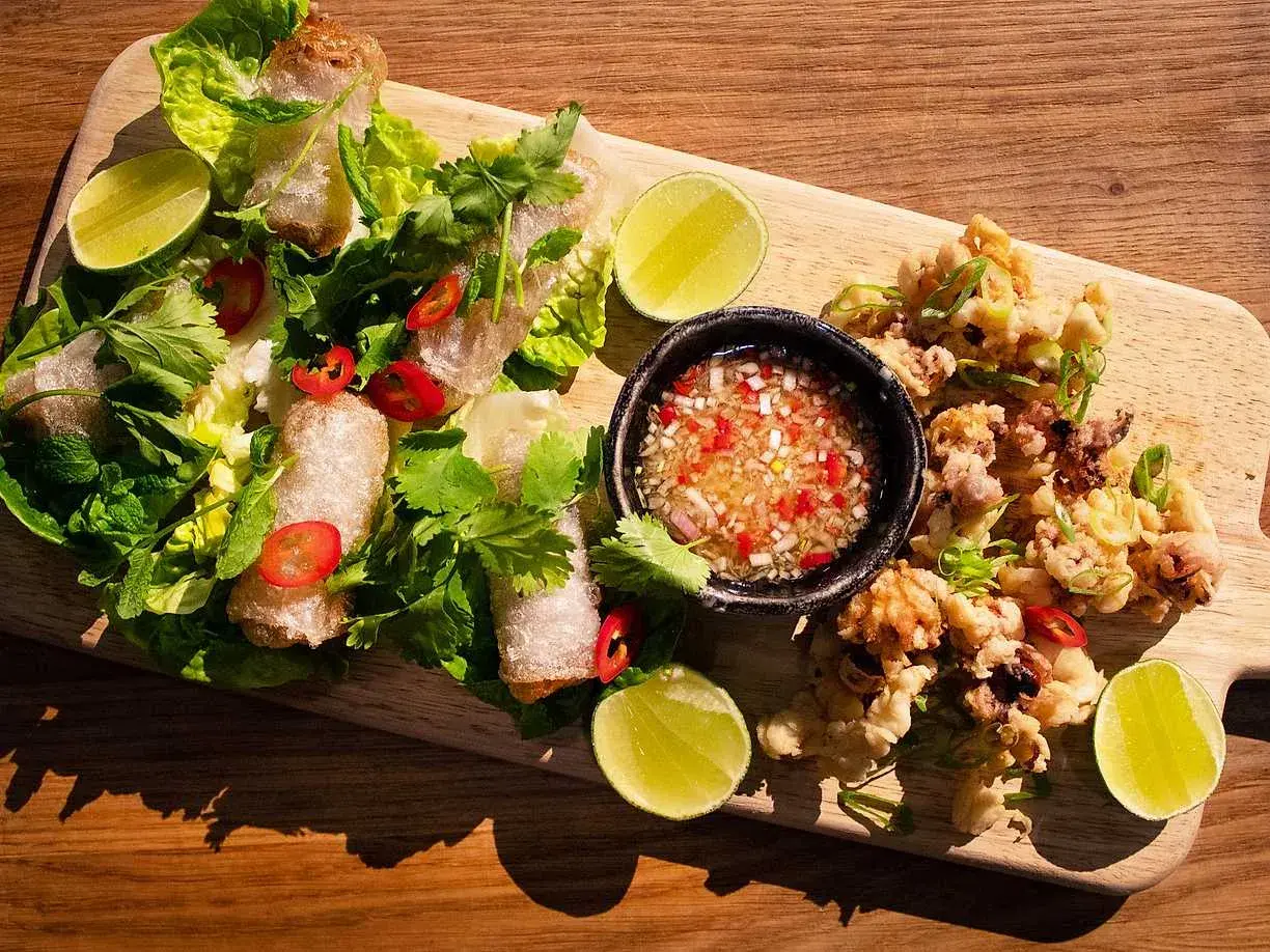 Krispiga cha gio med färska örter, lime och en dippsås. Bredvid ligger friterad bläckfisk.