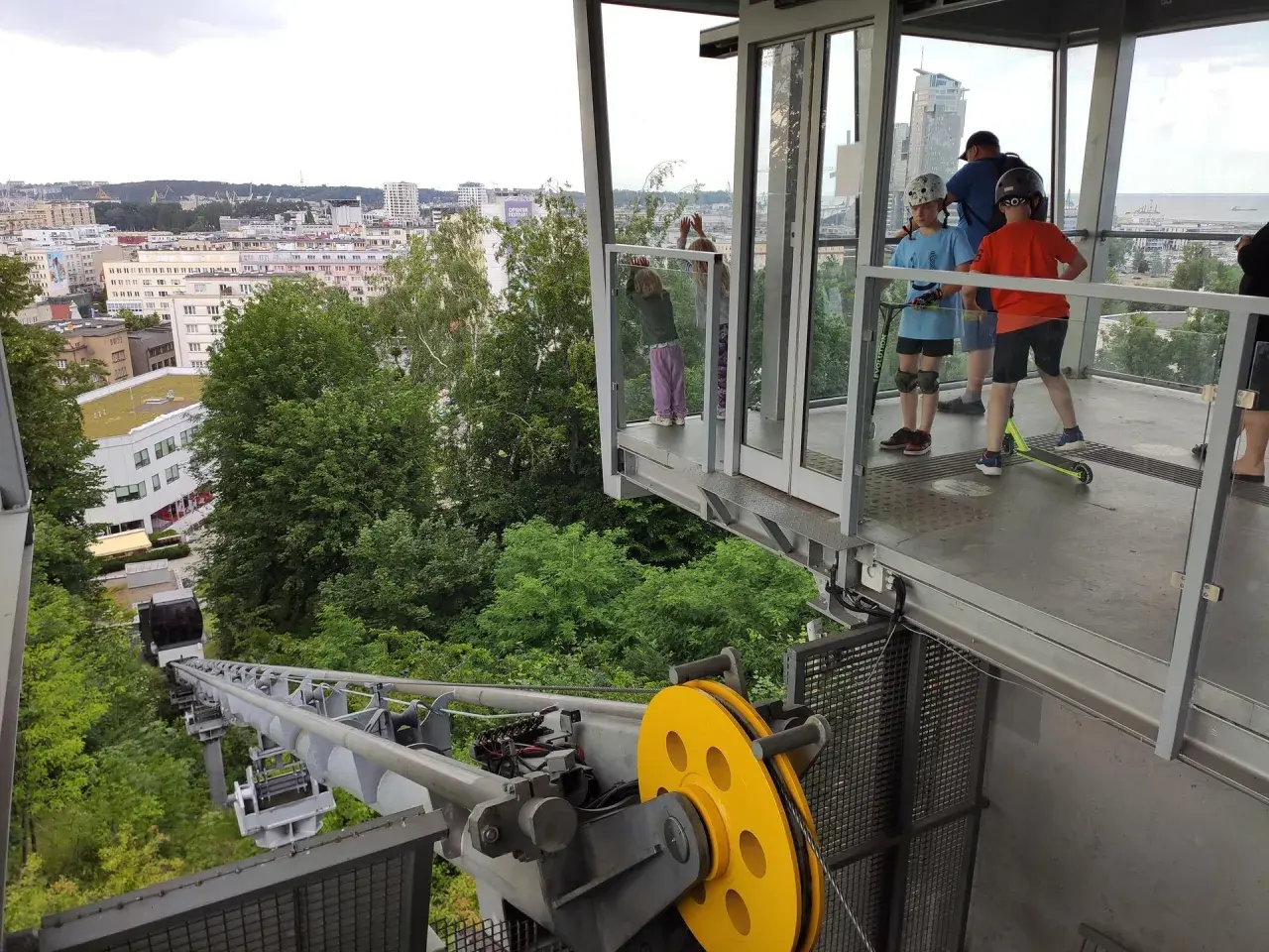 Dzieci z hulajnogami czekają na przejazd kolejką linową Gdynia. Widok na miasto i morze.