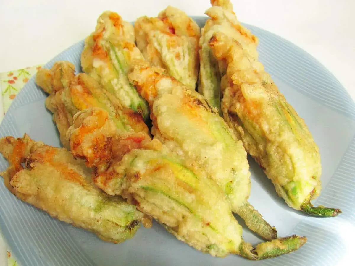 Fiori di zucca ripieni di ricotta, dorati e croccanti, serviti su un piatto azzurro.