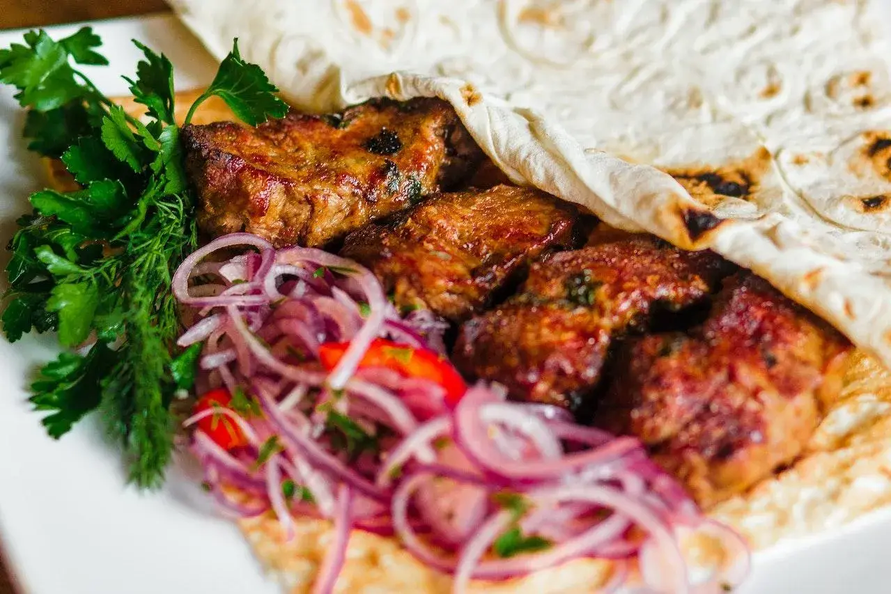 Soczyste mięso kebab zawinięte w placek, podane z czerwoną cebulą i świeżą natką pietruszki.