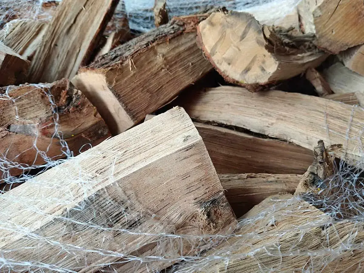 Gros tas de bois humide, prêt pour le poêle. Les bûches sont emballées dans un filet blanc.