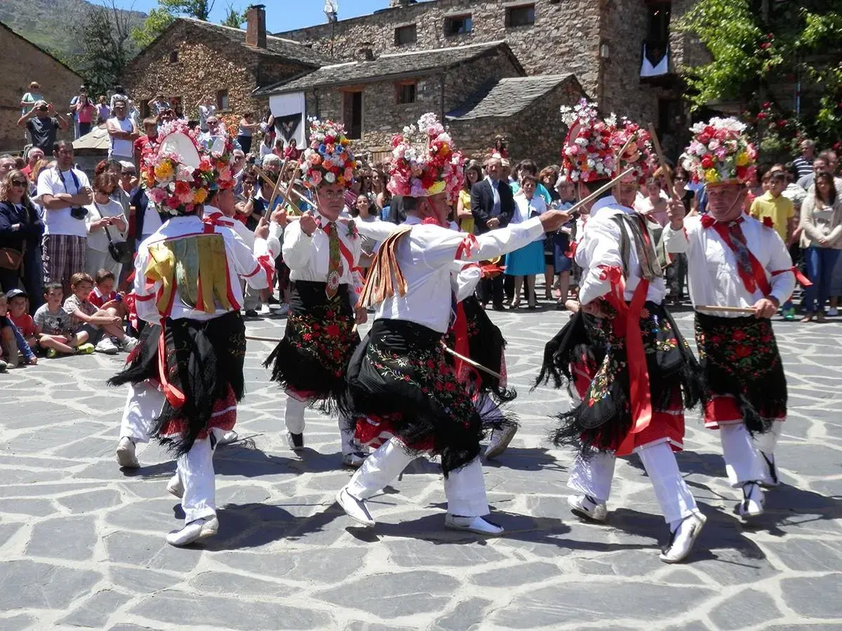 Hombres con trajes tradicionales y sombreros florales bailan en la plaza durante el **Día del Corpus**.