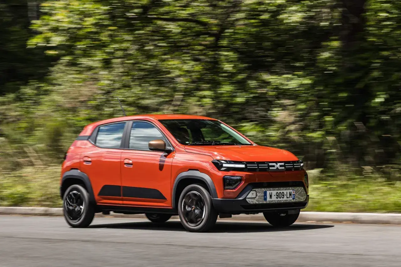 Auto arancione in movimento, con cambio automatico, su strada circondata da alberi sfocati.