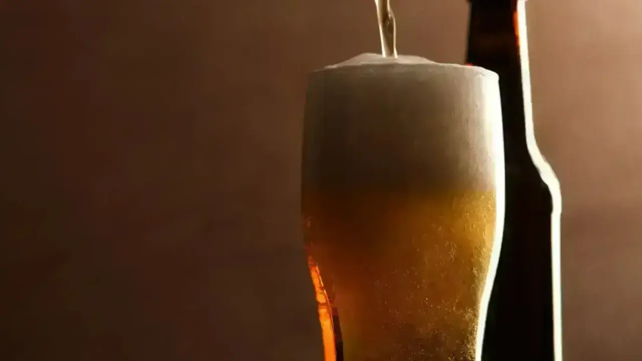 Birra inglese più famosa versata in un bicchiere con schiuma abbondante, accanto a una bottiglia scura.