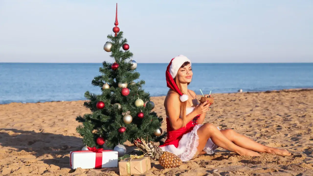 Kobieta w stroju Mikołaja pije koktajl na plaży obok choinki. Czy 28 grudnia jest dniem wolnym od pracy?