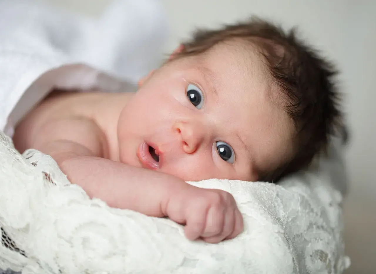 Un neonato con occhi spalancati, che sembra scoprire il mondo. La sua espressione curiosa cattura il momento in cui iniziano a vedere i neonati.