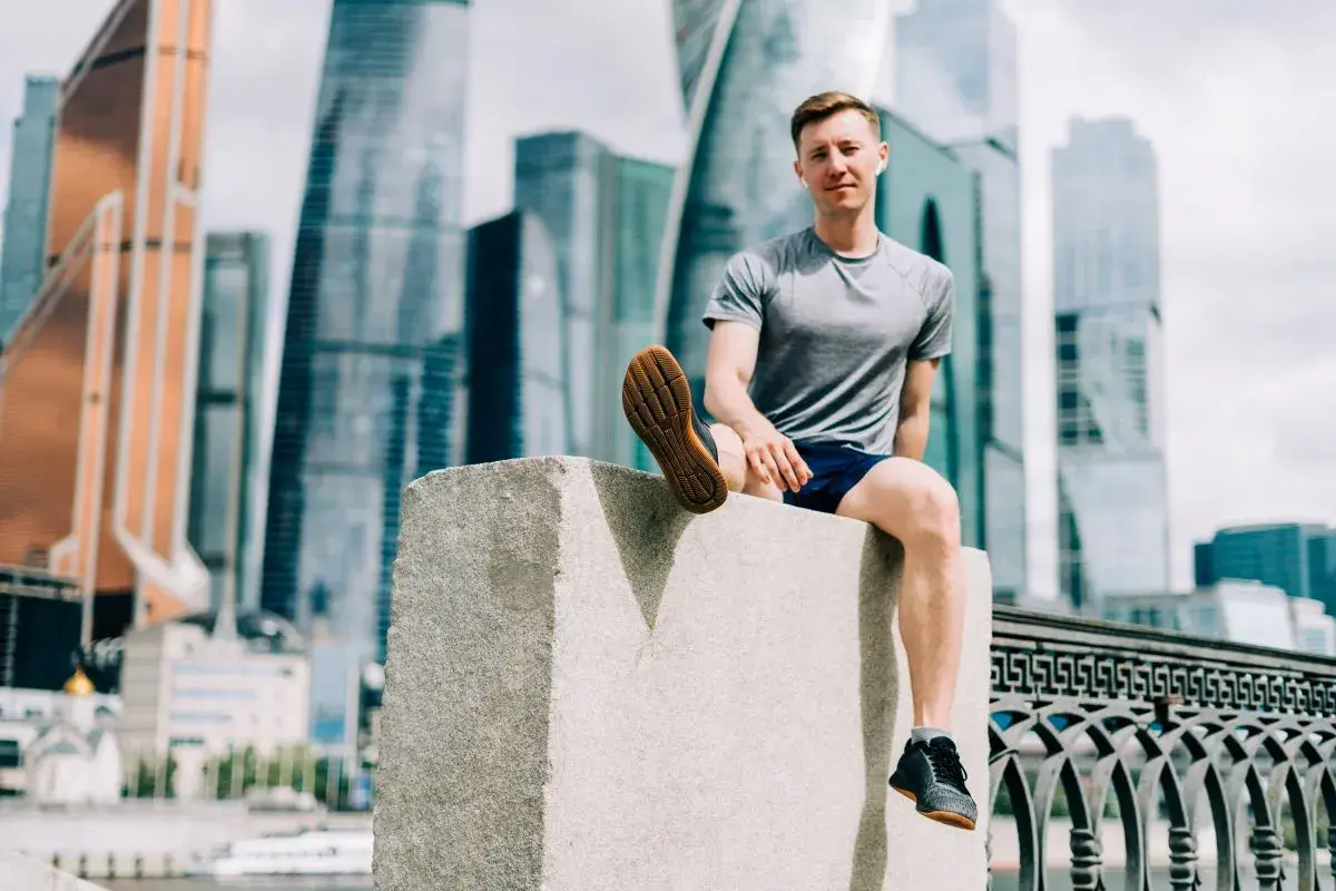 Mężczyzna w sportowym stroju siedzi na kamiennym postumencie, w tle nowoczesne wieżowce. Czasem czuję, że nie mogę złapać oddechu podczas biegania.