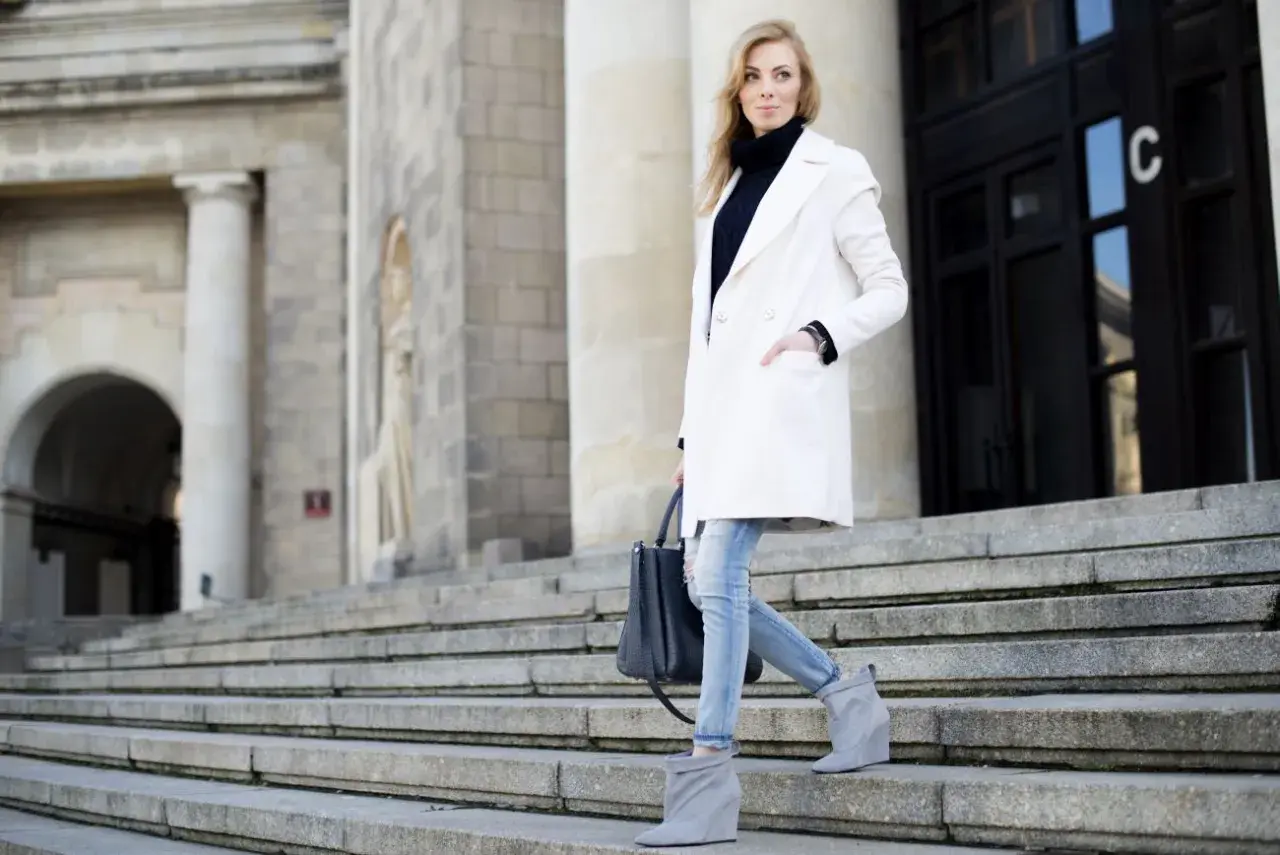 Elegancka kobieta w białym płaszczu i jeansach schodzi po schodach. Stylowe biały płaszcz stylizacje na co dzień.