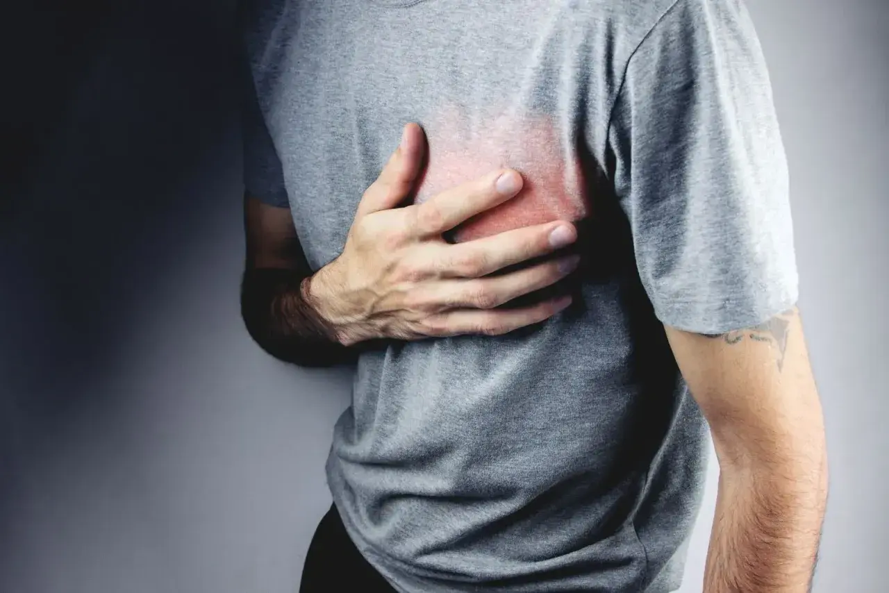 Mężczyzna trzyma się za klatkę piersiową, odczuwając ból. Czerwony obszar na jego koszulce sugeruje nerwobóle serca.