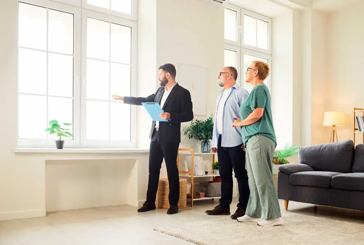 Agente inmobiliario explica a pareja cuánto dura una tasación, señalando la luz natural de la vivienda.