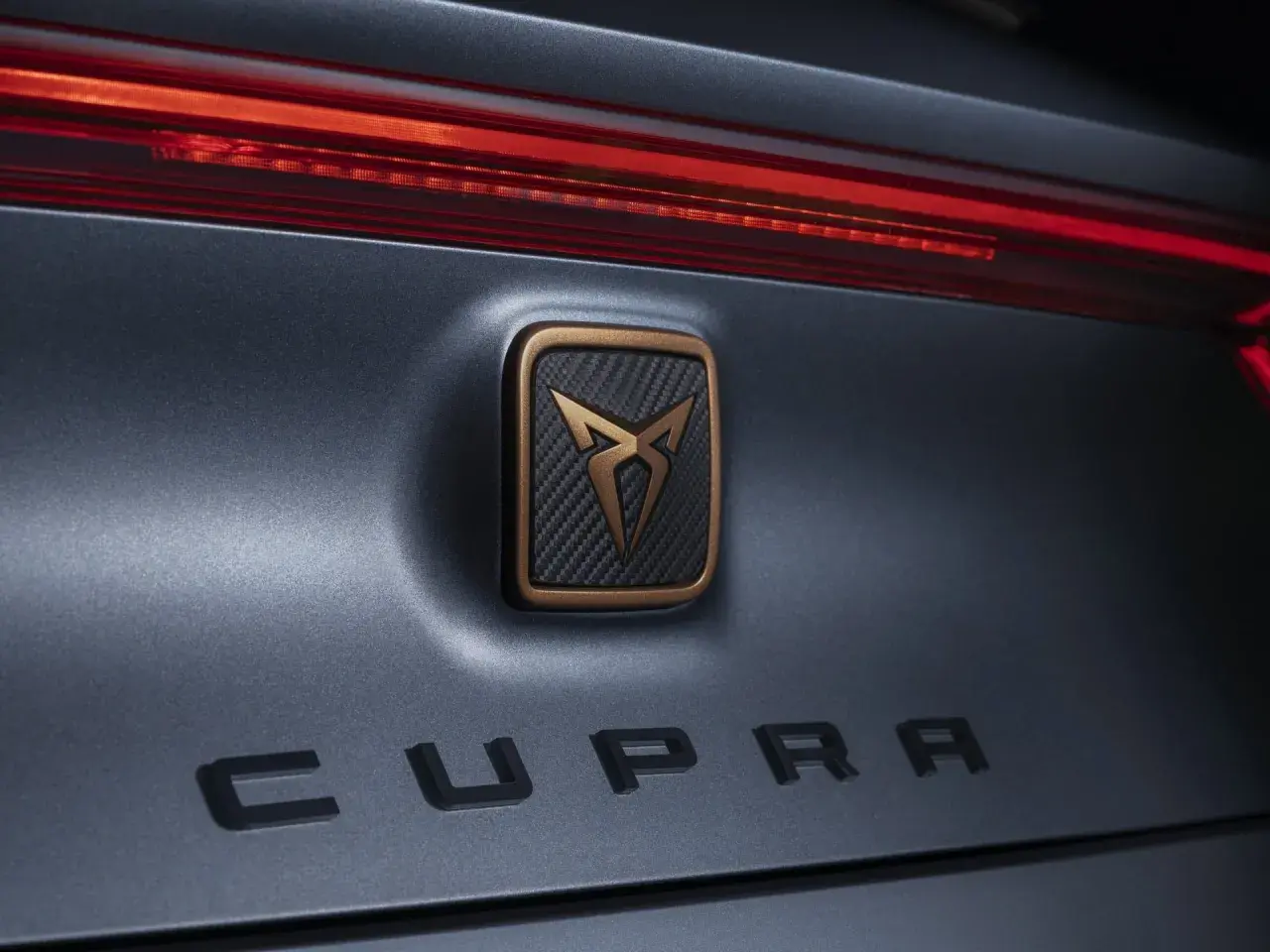 Dettaglio posteriore di un'auto Cupra, con logo in bronzo e carbonio e scritta "CUPRA" in rilievo. Un omaggio al suo **seat origine**.