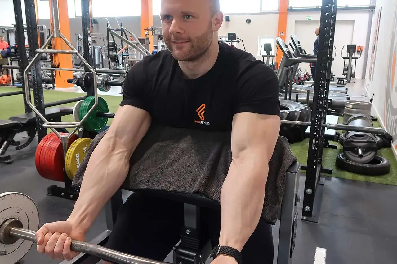 Mann trainiert Bizeps mit Langhantel im Fitnessstudio. Deutlich sichtbare Muskeln beim Bizeps dehnen.