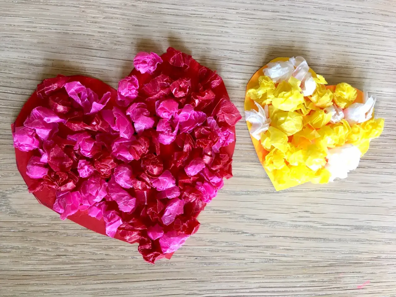 Zwei bunte Herzen, rot und gelb, mit zerknülltem Seidenpapier beklebt. Ein schönes Beispiel für herz basteln kinder.