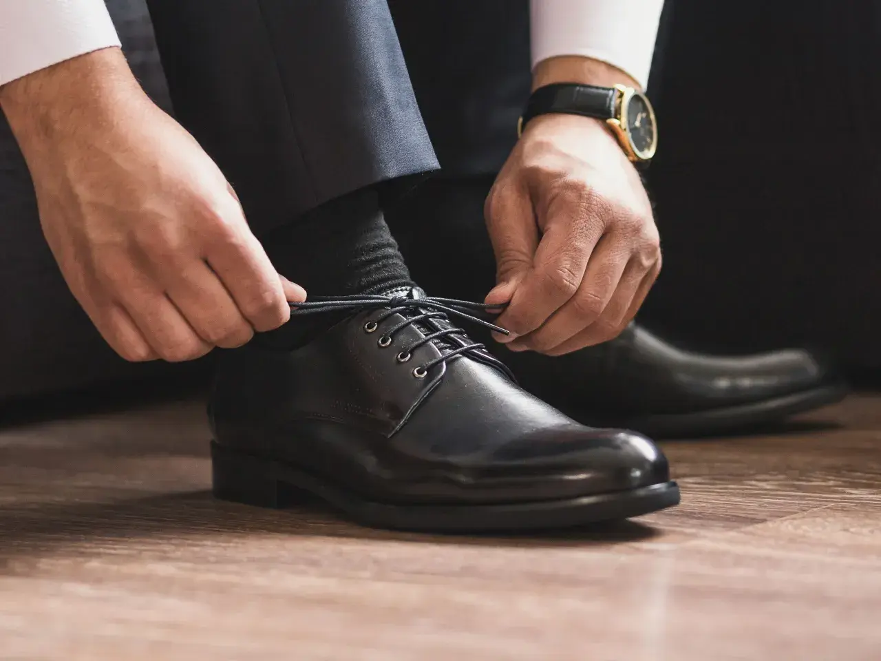 Mann schnürt schwarze Anzugschuhe. Die Wahl der richtigen Socken zum Anzug ist entscheidend für einen perfekten Look.