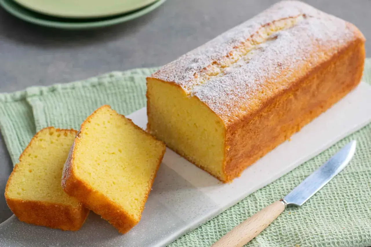 Un soffice plumcake yogurt, spolverato di zucchero a velo, pronto per essere gustato. Due fette sono già state tagliate.