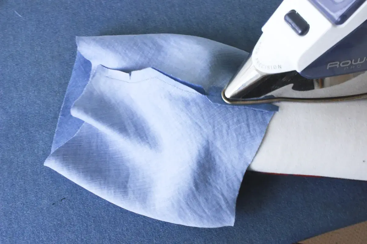 Ironing a folded cuff band to a light blue sleeve. This step is crucial for how to sew a folded cuff band to a sleeve.
