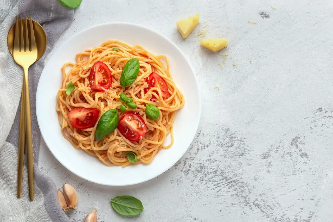Leckere Tagliatelle Rezepte: Spaghetti mit Tomaten, Basilikum und Parmesan auf einem Teller, daneben goldene Gabel und Messer.
