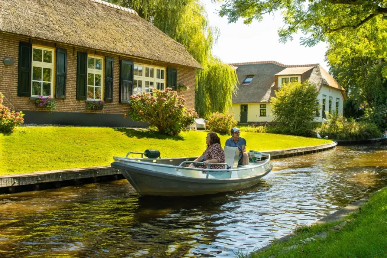Ein Paar genießt eine Bootsfahrt durch das malerische Klein Venedig Holland, vorbei an reetgedeckten Häusern und üppigem Grün.