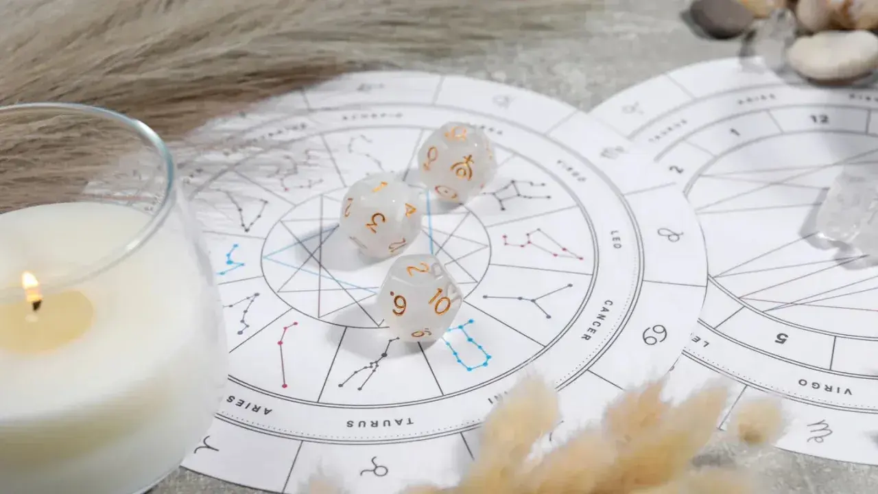 Karty zodiaku, kostki z symbolami planet i płonąca świeca tworzą mistyczną atmosferę.