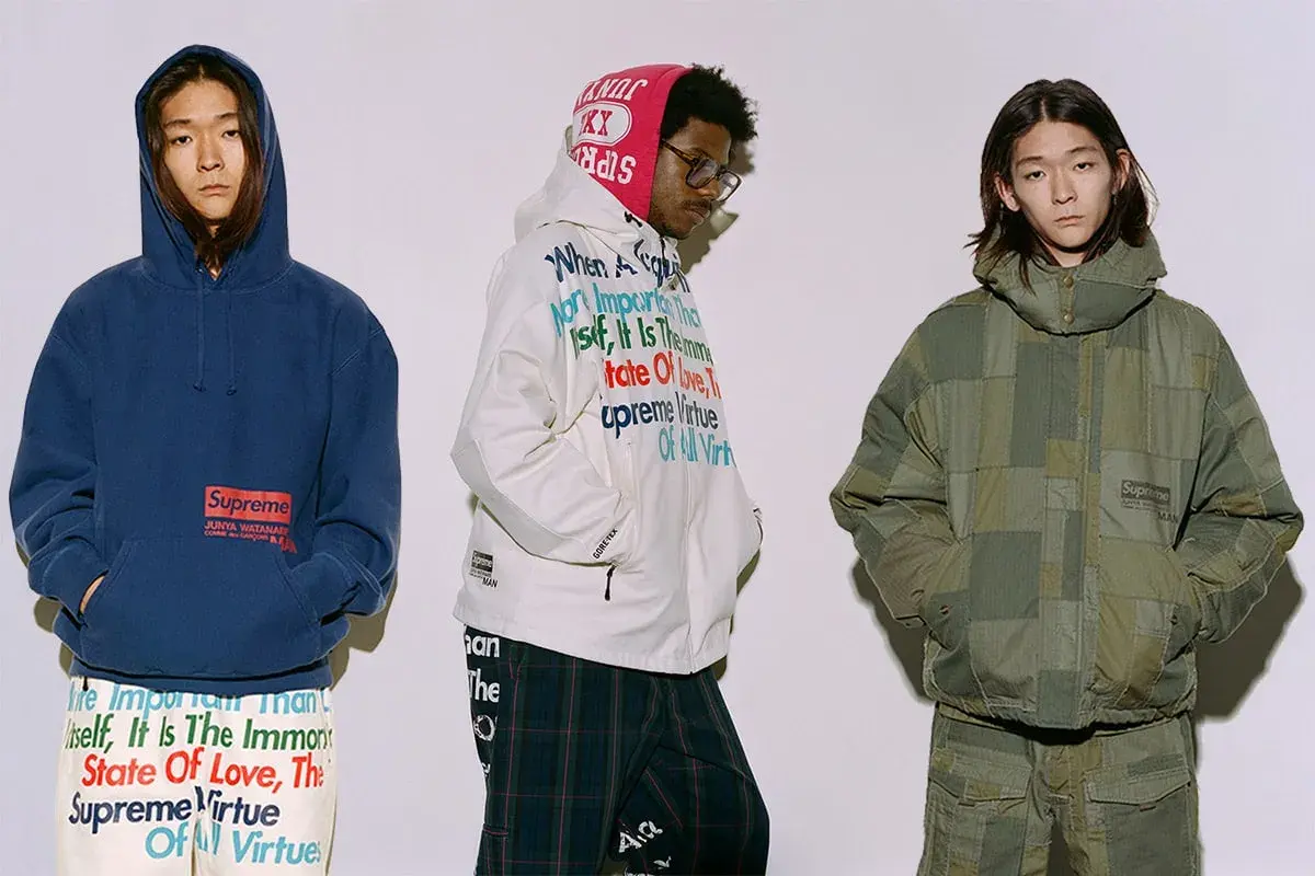 Trzech mężczyzn w ubraniach z kolekcji Junya Watanabe x Supreme. Jeden w granatowej bluzie, drugi w białej kurtce z tekstem, trzeci w zielonej, patchworkowej kurtce.