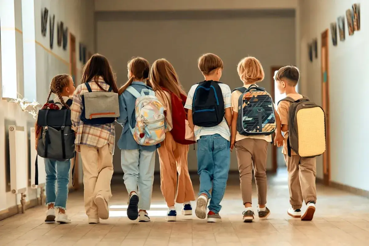Dzieci z plecakami idą korytarzem. Czas na wystawienie ocen na 1 semestr!