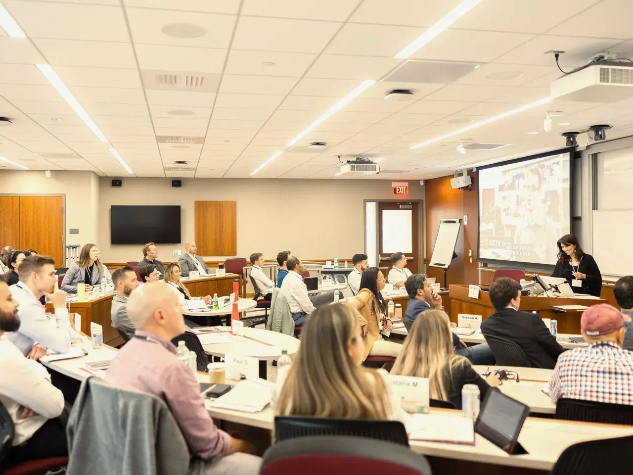Attendees at negotiation seminars listen intently to a speaker presenting on a large screen.