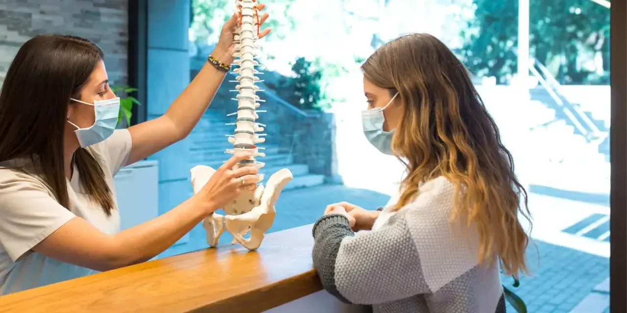 Fizjoterapeuta wyjaśnia pacjentce model kręgosłupa, omawiając, czy z przepukliną kręgosłupa można pracować.