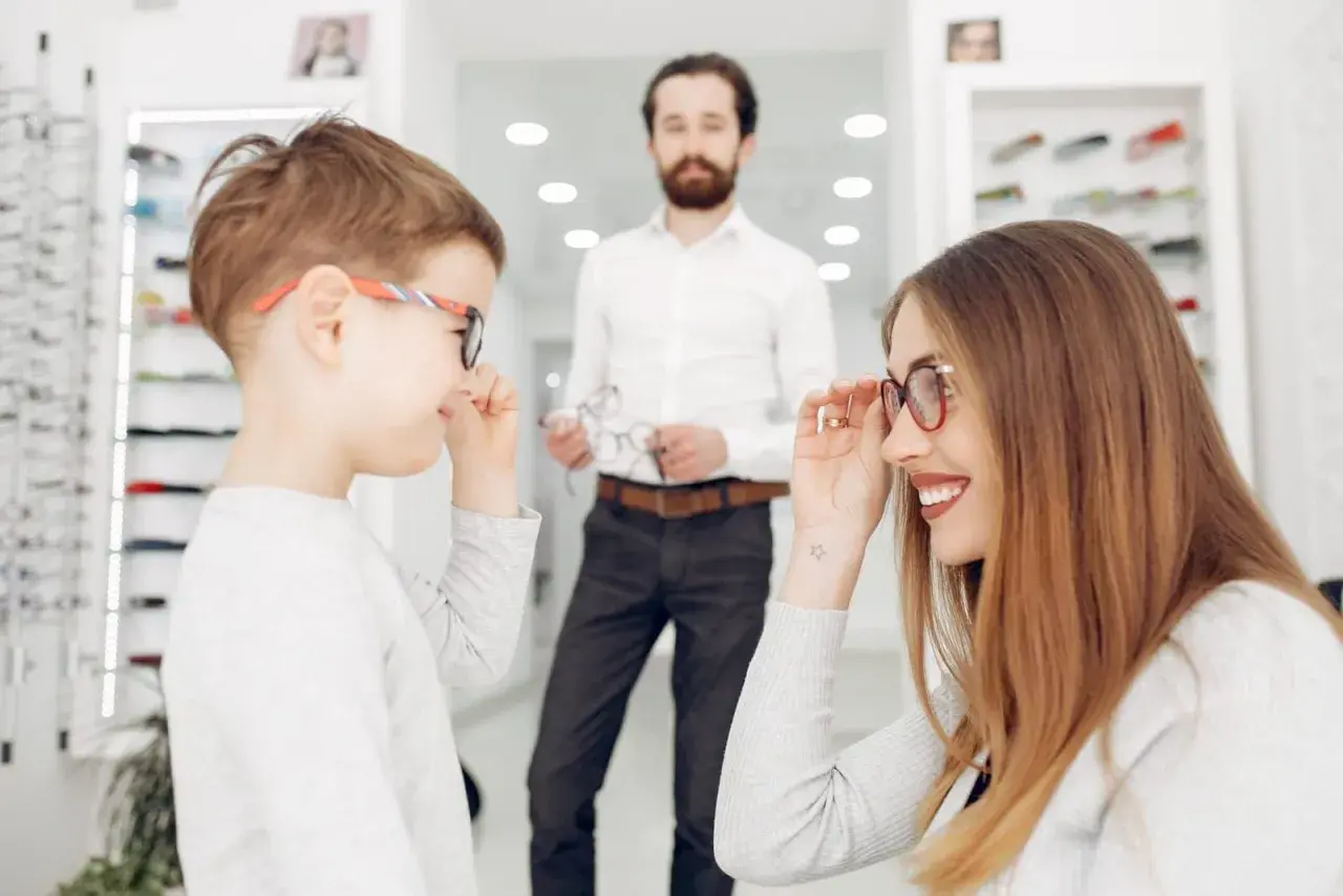 Niños probándose gafas en una óptica. La madre ayuda a su hijo con un **ojo vago** a elegir montura.