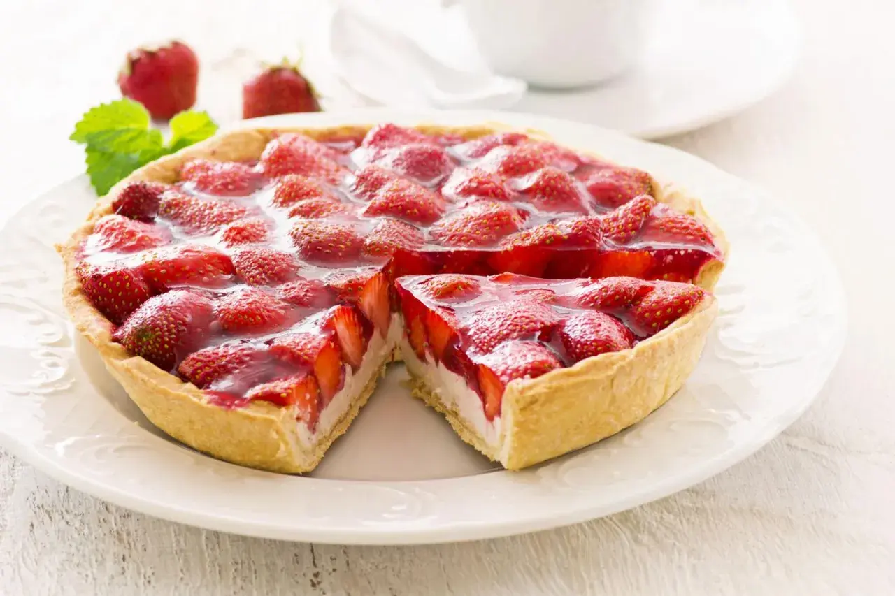 Ein saftiger Erdbeerkuchen mit Quarkfüllung, bedeckt mit frischen Erdbeeren und glänzendem Tortenguss. Ein Stück ist bereits entnommen.