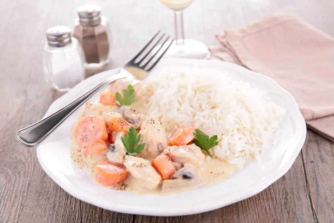 Une assiette de blanquette de veau crémeuse avec des carottes et des champignons, servie avec du riz blanc. Un verre de vin de Bordeaux est suggéré pour accompagner ce plat.