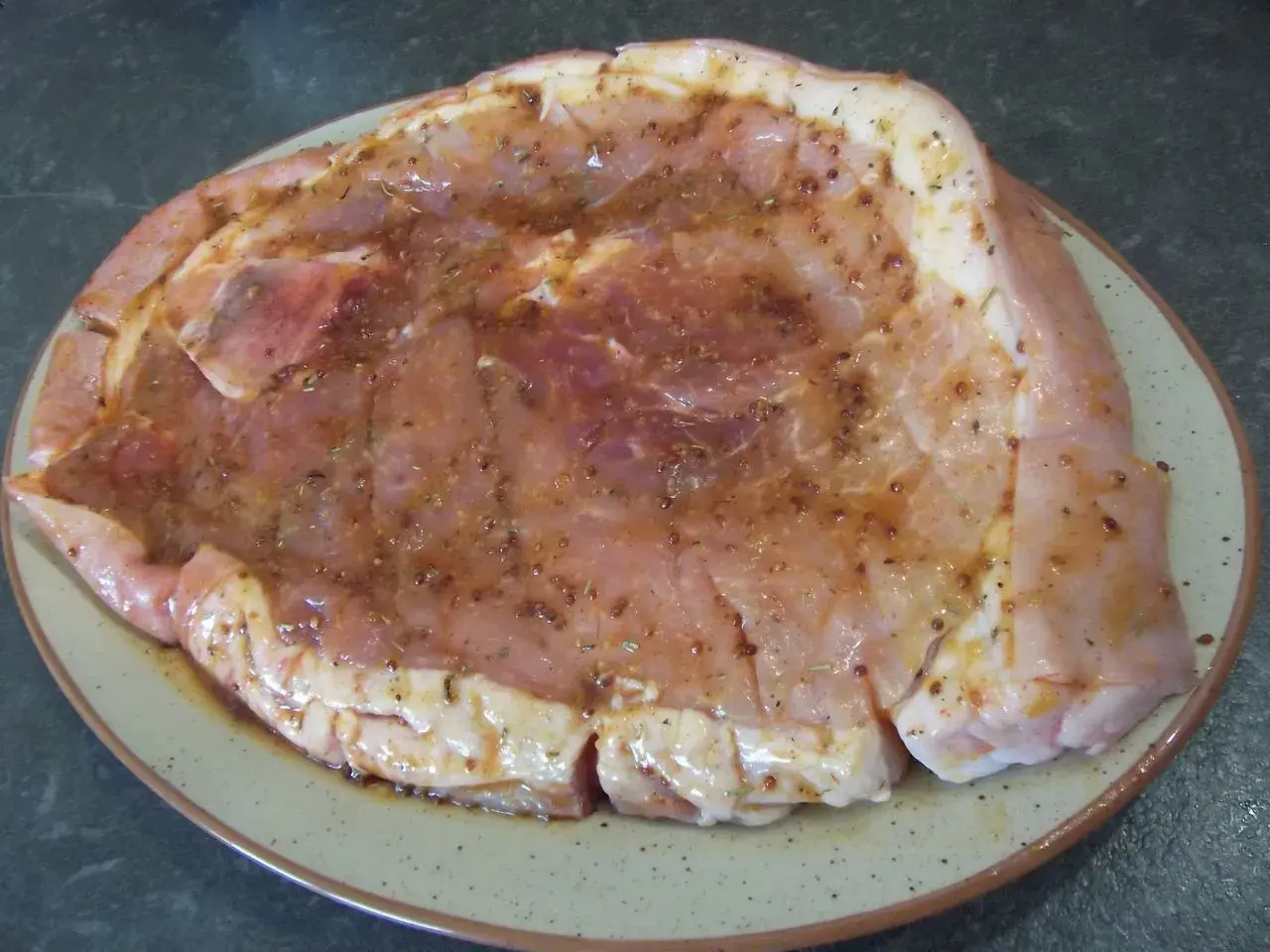 Rouelle de porc prête pour la plancha, généreusement recouverte d'une marinade savoureuse aux herbes et épices.
