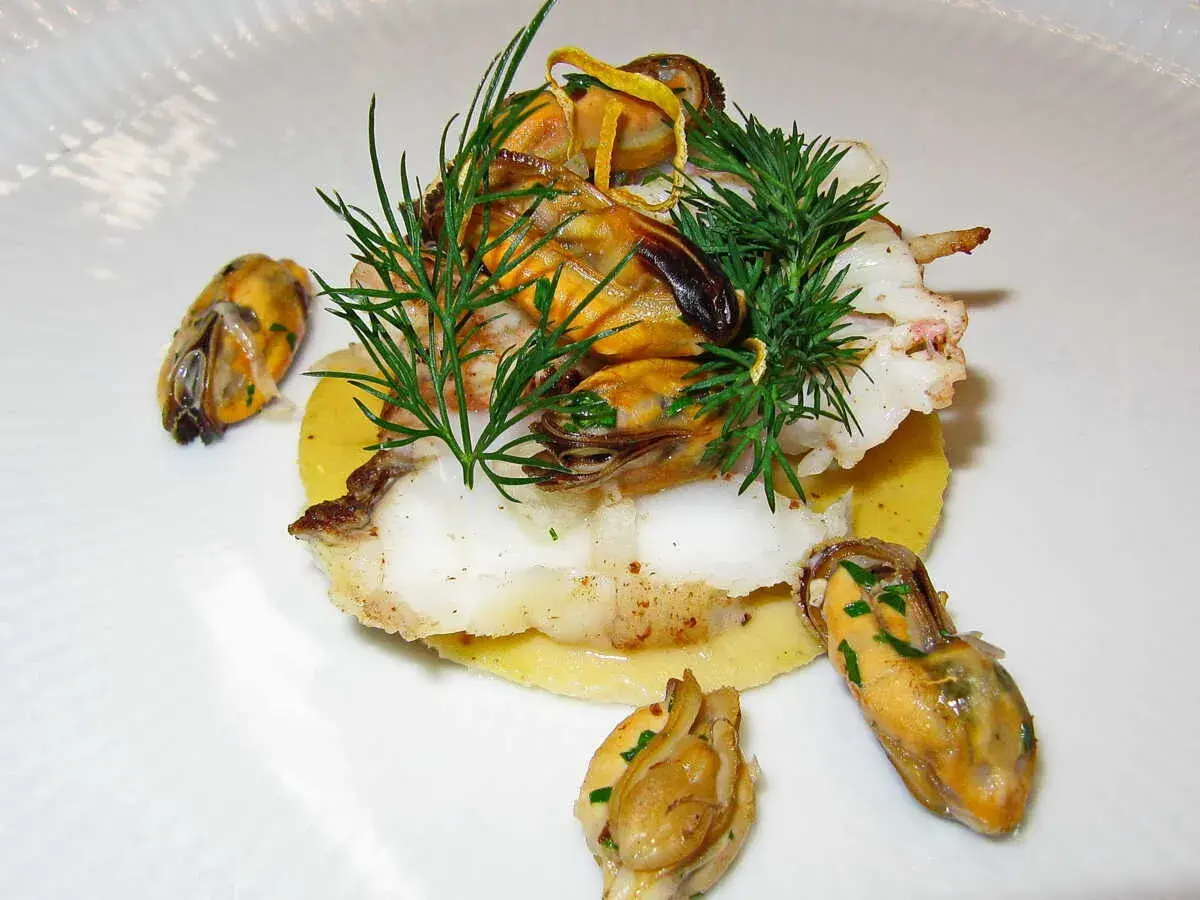 Délicieux plat de joue de lotte poêlée, garni de moules et d'aneth frais, servi sur un lit de purée.