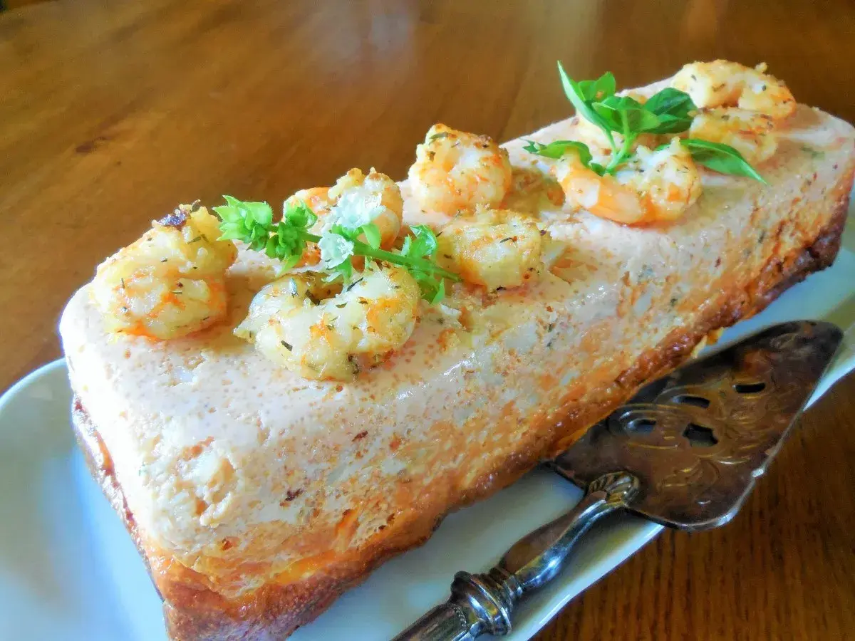 Un délicieux pain de poisson aux crevettes et herbes fraîches, prêt à être découpé avec une pelle à tarte ornée.