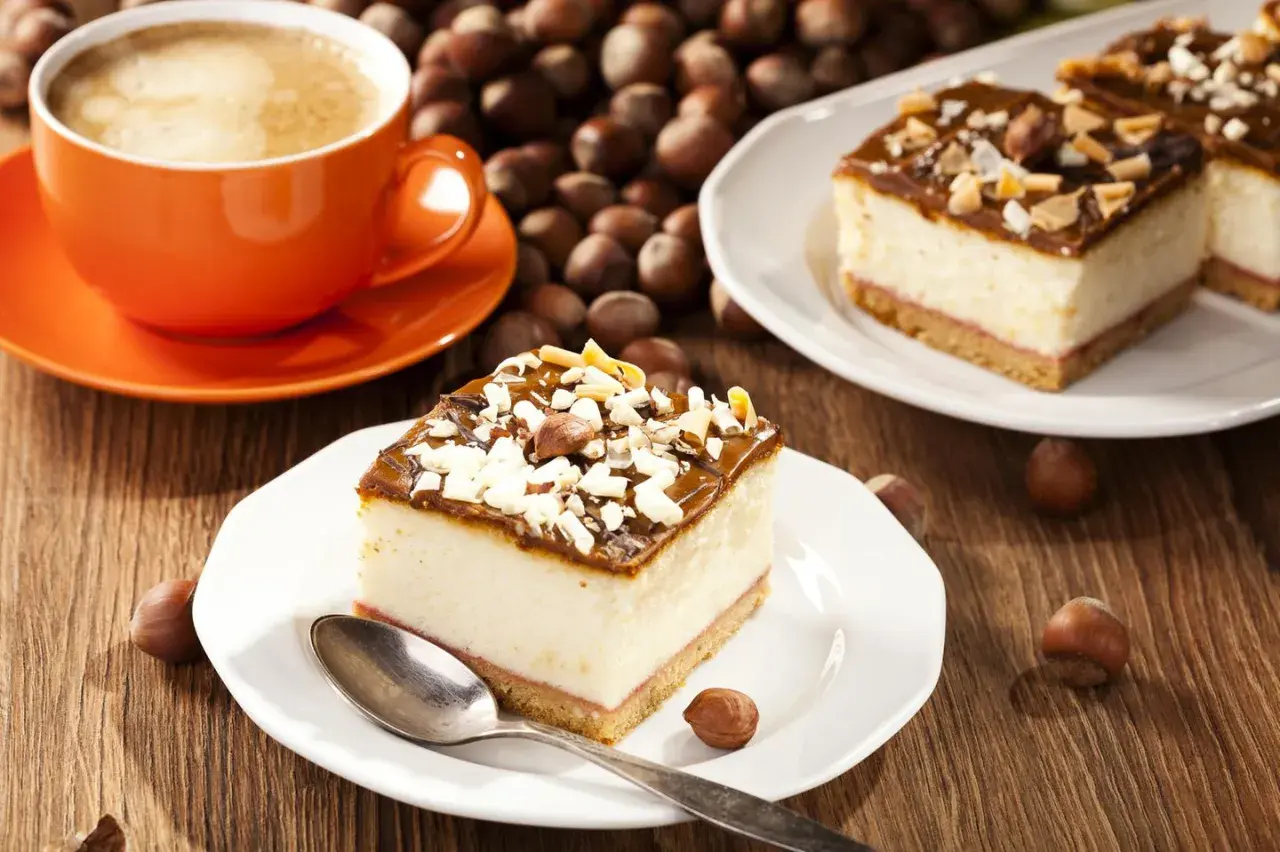 Ein Stück cremiger Käsekuchen mit Schokoladenglasur und Nüssen, dazu eine Tasse Kaffee. Perfekt für einen schnellen Kuchengenuss.