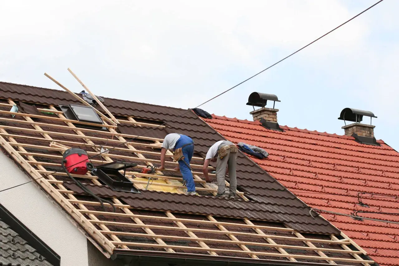 Deux couvreurs travaillent sur une toiture en cours de rénovation, préparant à prolonger un toit existant.
