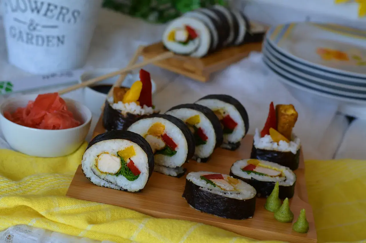 Pyszne sushi z kurczakiem, papryką i mango na desce. Obok miseczka z imbirem i sos sojowy.