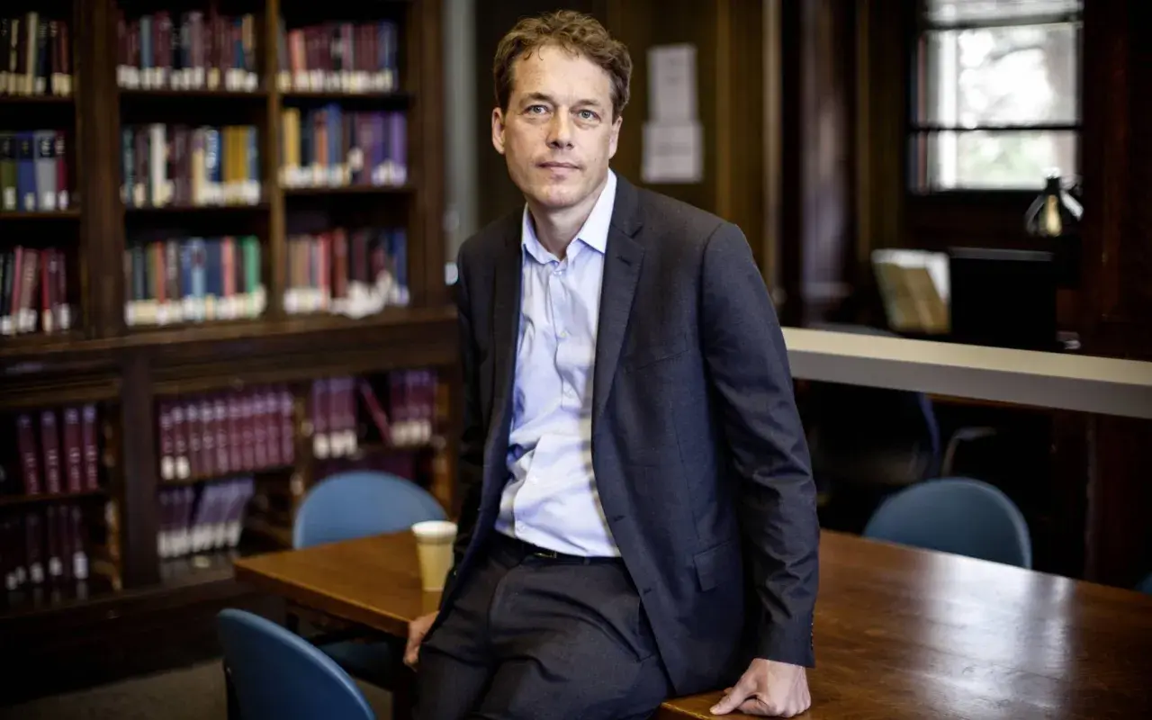 Sven Beckert sitzt in einer Bibliothek, umgeben von Büchern.