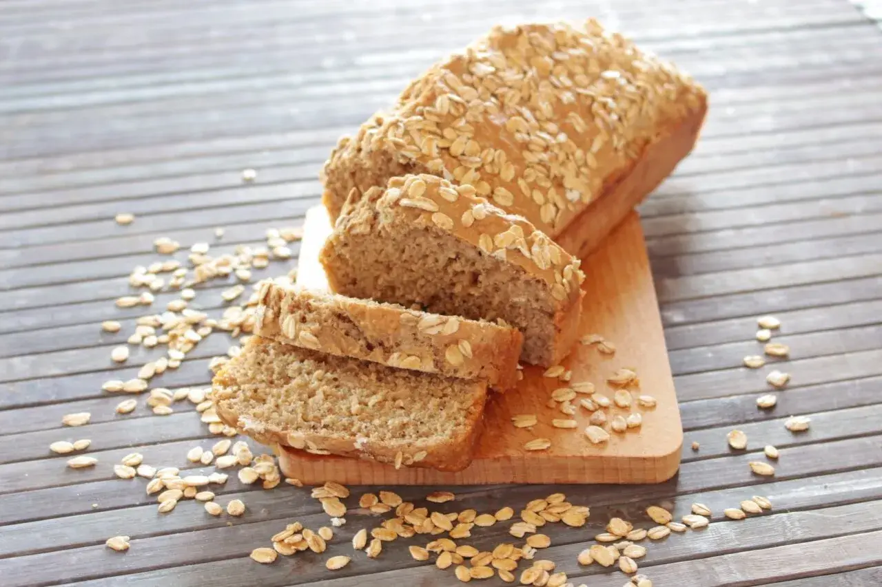 Pane proteico integrale, cosparso di fiocchi d'avena, affettato su un tagliere di legno.