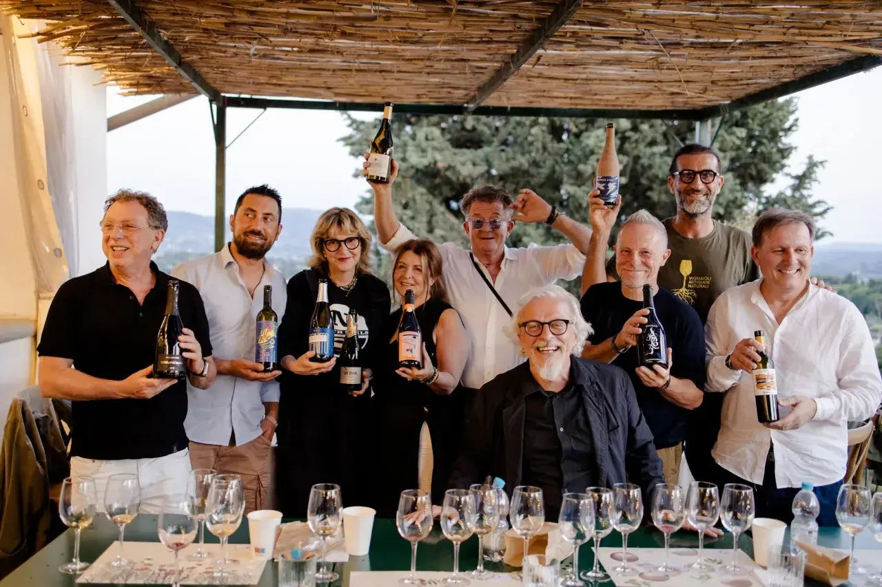 Un gruppo di persone sorridenti, alcuni con bottiglie di vino, celebra i papi marchigiani.
