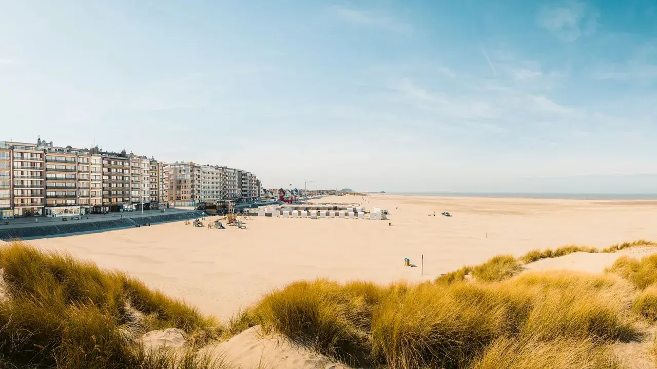 Breiter Sandstrand mit Dünen und Strandkörben in Belgien, Knokke. Lange Häuserzeile am Boulevard.