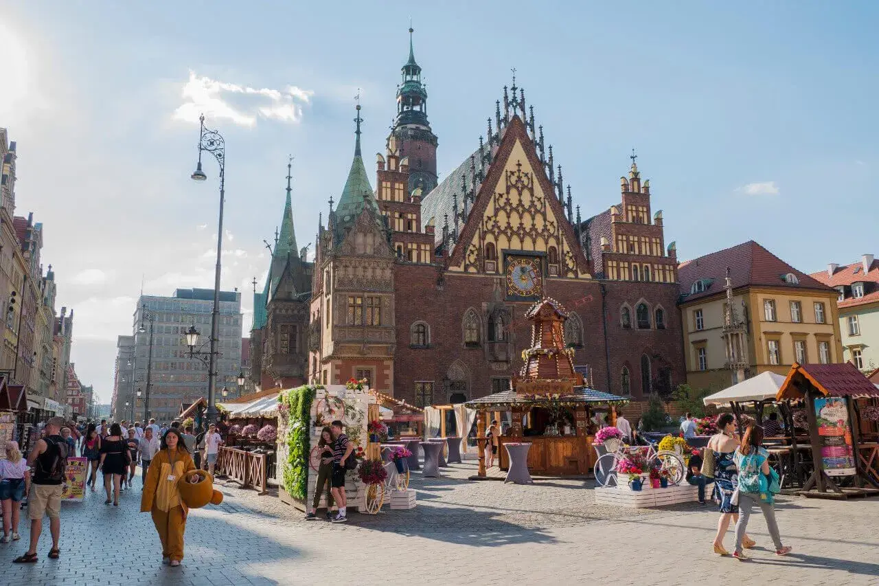 Tętniący życiem Rynek we Wrocławiu, z pięknym Ratuszem i kramami pełnymi kwiatów. Wspaniałe wrocławskie atrakcje w letnim słońcu.