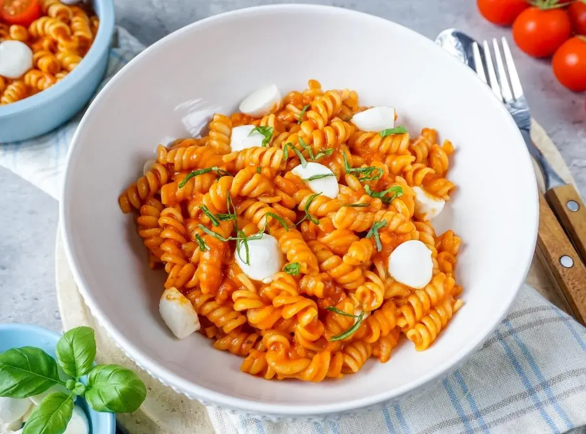 Eine Schüssel mit köstlicher One Pot Pasta, Fusilli in Tomatensauce mit Mozzarella-Kugeln und frischem Basilikum garniert.