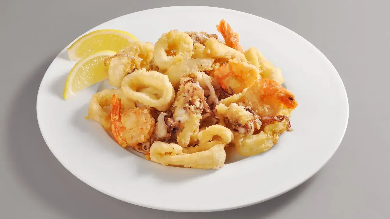 Un invitante piatto di frittura di pesce, con anelli di calamari dorati e gamberi croccanti, guarnito con spicchi di limone fresco.