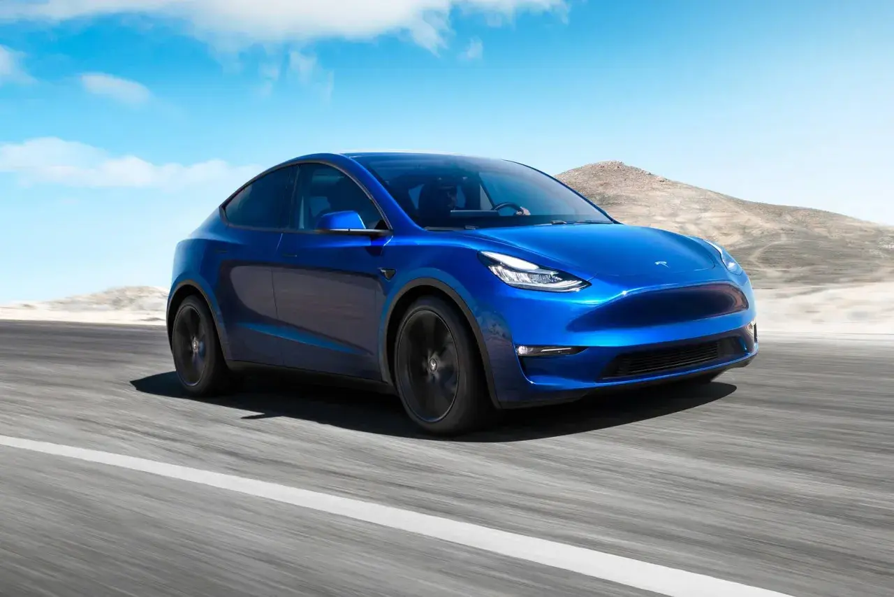 Blå Tesla Model Y kör på en väg i ökenlandskap. En dröm om en tesla till salu.