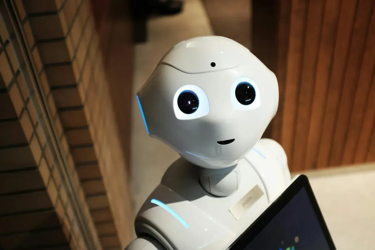 Der humanoide Roboter Pepper mit leuchtenden Augen und blauen Akzenten hält ein Tablet. Er ist bereit für eine audio ki-gesteuerte Interaktion.
