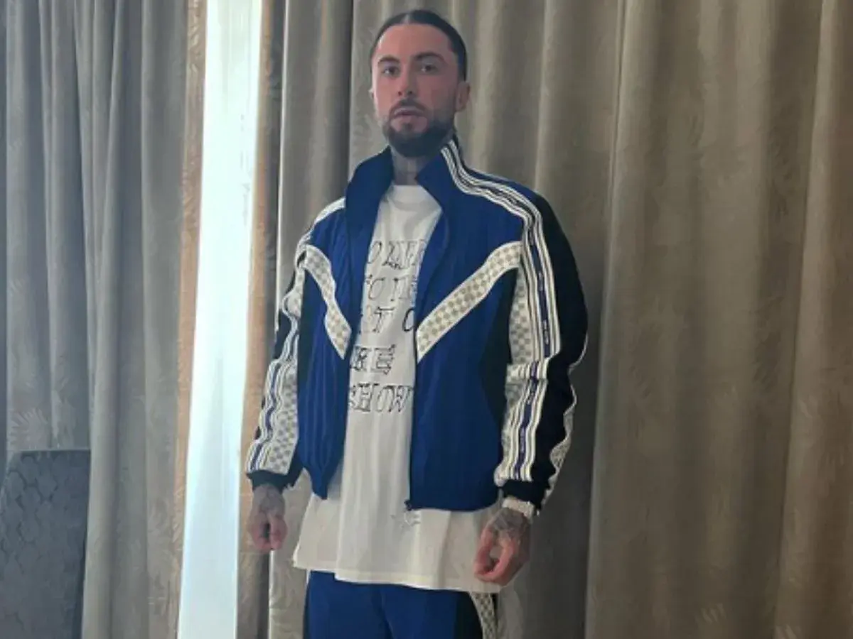Malik Montana w niebieskiej kurtce i białej koszulce, gotowy na spotkanie z malik montana dzieci.
